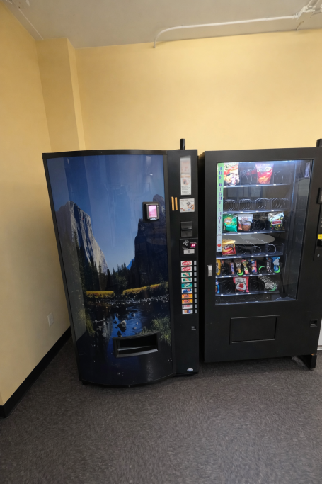 Two vending machines side by side in a small room with beige walls.